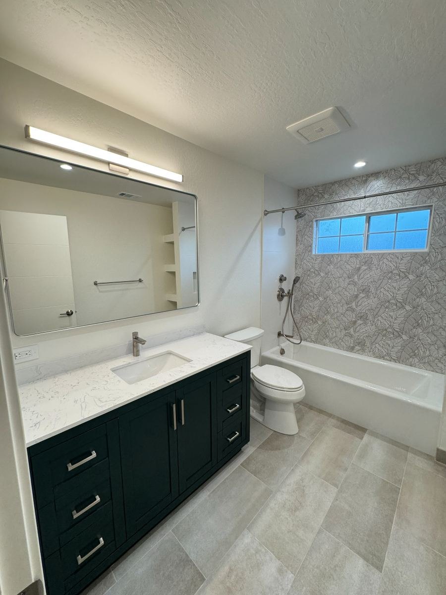 Bathroom remodel with green vanity, lit mirror and tiled tub surround